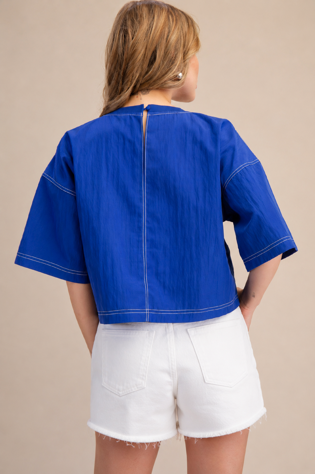 Person wearing a blue top and white shorts on a beige background