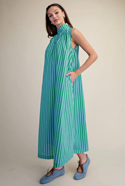A woman modeling a sleeveless, high-neck maxi dress with vertical mint green and white stripes, paired with light blue lace-up shoes, against a solid beige studio background.