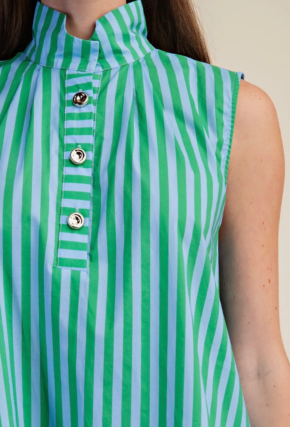Close-up of a sleeveless high-neck top with vertical green and light blue stripes, featuring a button placket with silver-tone buttons.