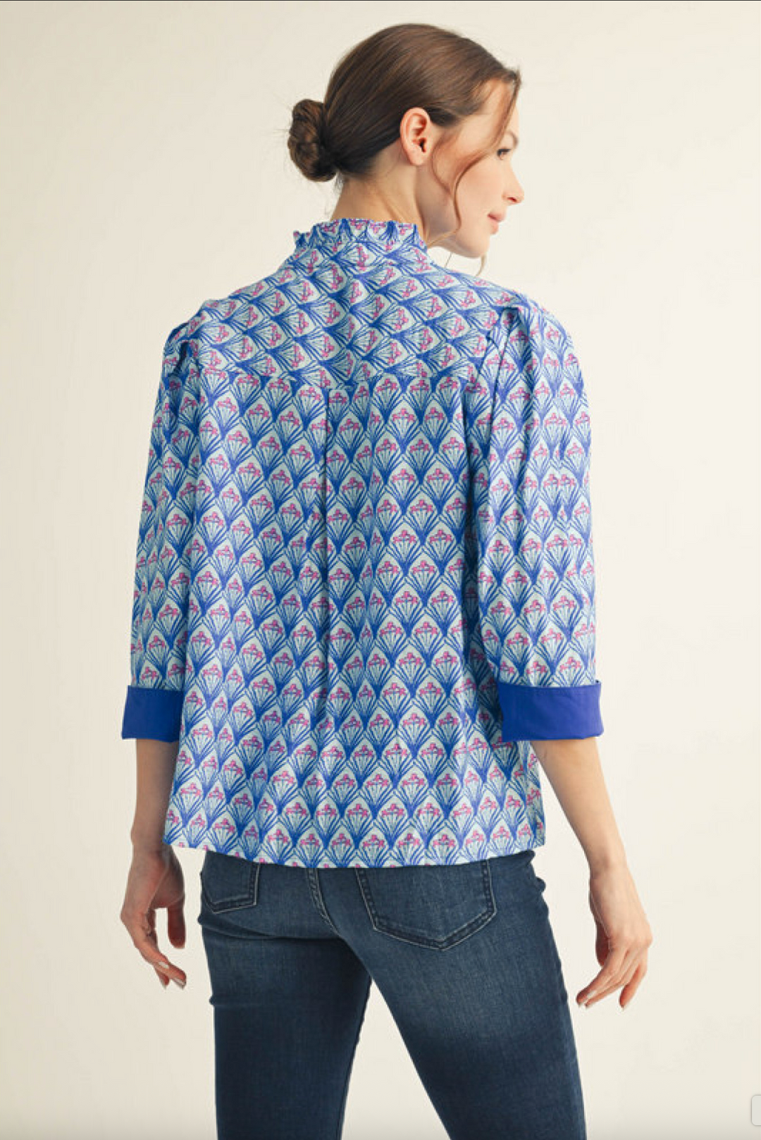 Woman wearing a blue patterned blouse with cuffed sleeves and dark denim jeans, back view
