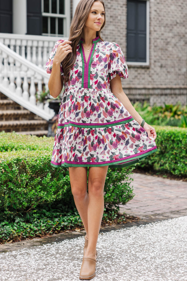 Woman wearing a floral print mini dress with puff sleeves and green trim, outdoors by a brick house.