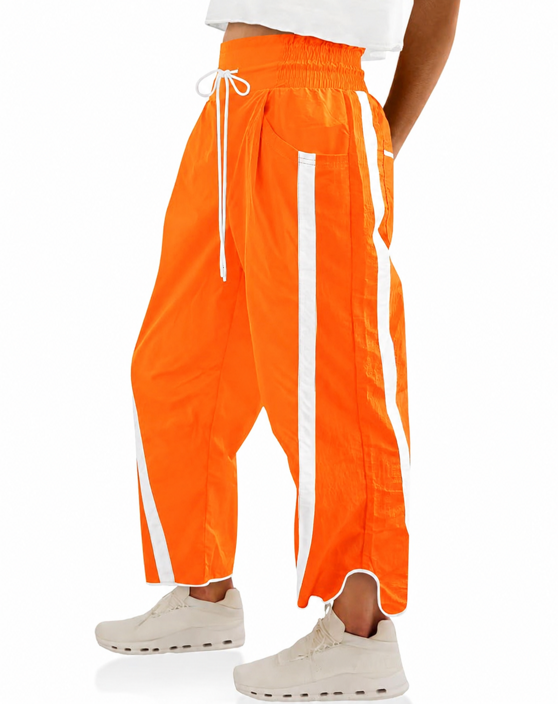 Bright orange wide-leg track pants with white side stripes and a white drawstring waist, shown on a model from the waist down wearing off-white sneakers against a white background.