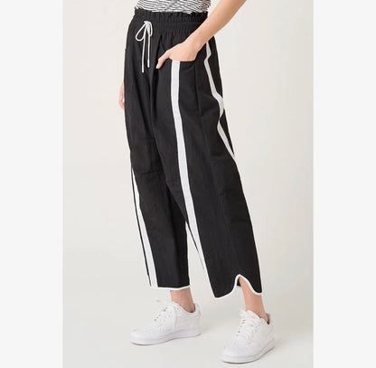 Black wide-leg cropped pants with white side stripes and a white drawstring waist, shown on a model wearing white sneakers against a light gray studio background.