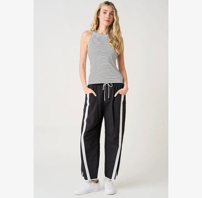 A woman modeling a sleeveless gray and white striped tank top with black wide-leg sweatpants featuring white side stripes, paired with white sneakers, against a light gray studio background.