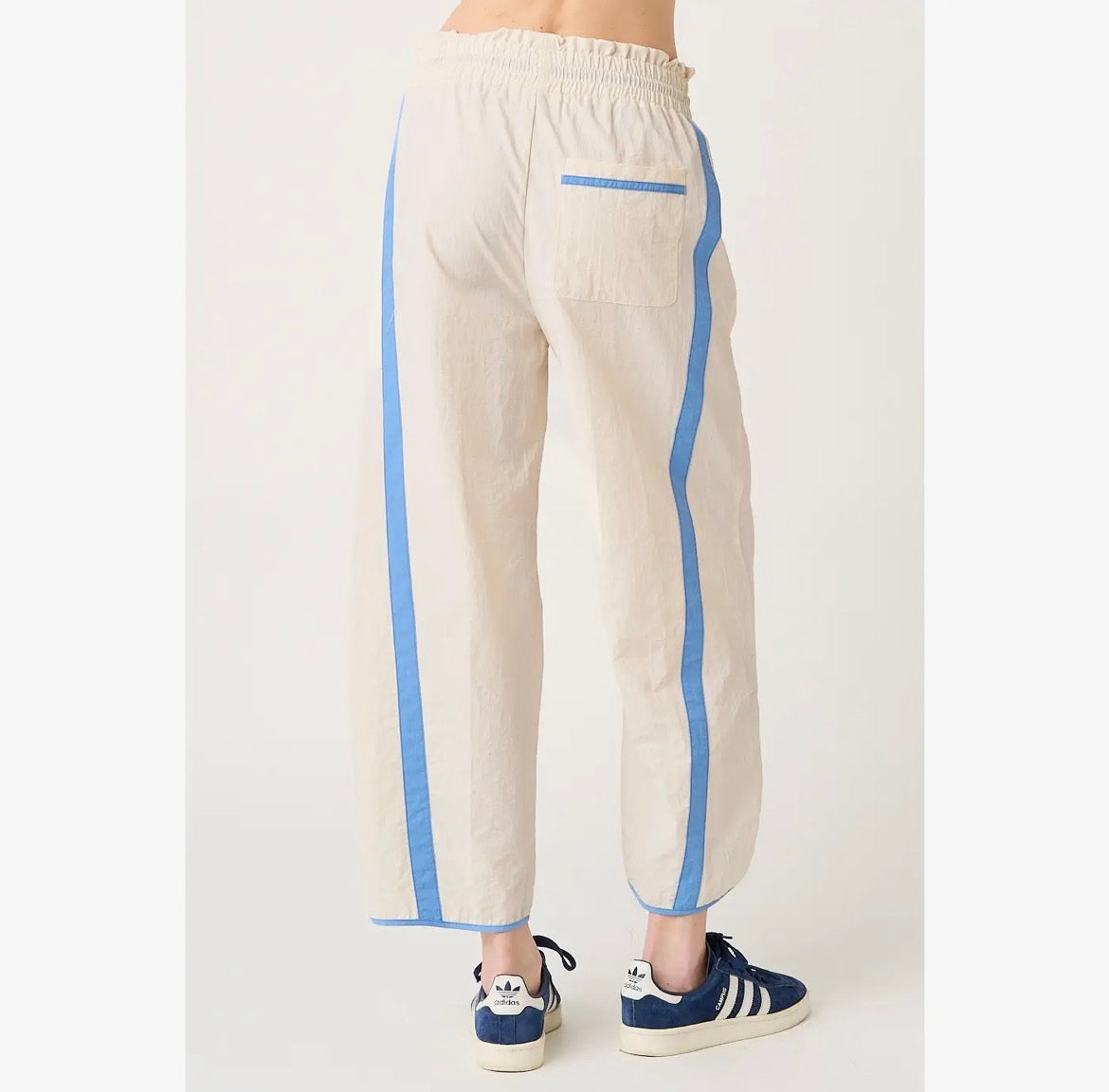 A person shown from the back wearing cream-colored linen pants with light blue side stripes and a matching back pocket, paired with blue sneakers.