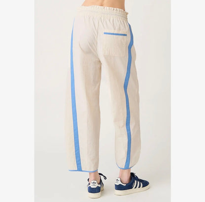 A person shown from the back wearing cream-colored linen pants with light blue side stripes and a matching back pocket, paired with blue sneakers.
