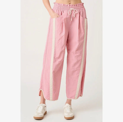 A person wearing pink wide-leg cropped pants with cream side panels and white sneakers, shown against a plain light background.