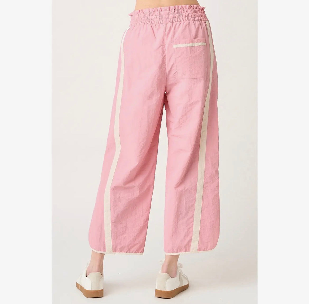 Pink wide-leg cropped pants with cream-colored side stripes and a back pocket, shown on a model from the back against a light gray background.