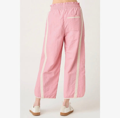 Pink wide-leg cropped pants with cream-colored side stripes and a back pocket, shown on a model from the back against a light gray background.