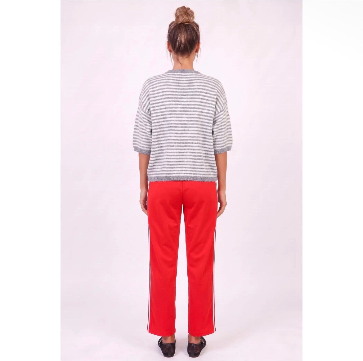 A person standing with their back to the camera, wearing a gray and white horizontally striped short-sleeve knit top and bright red wide-leg pants with white side stripes, set against a plain light background.