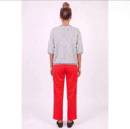 A person standing with their back to the camera, wearing a gray and white horizontally striped short-sleeve knit top and bright red wide-leg pants with white side stripes, set against a plain light background.