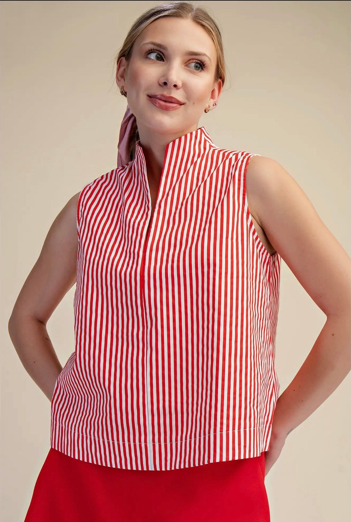 Woman wearing a red and white striped sleeveless top against a beige background