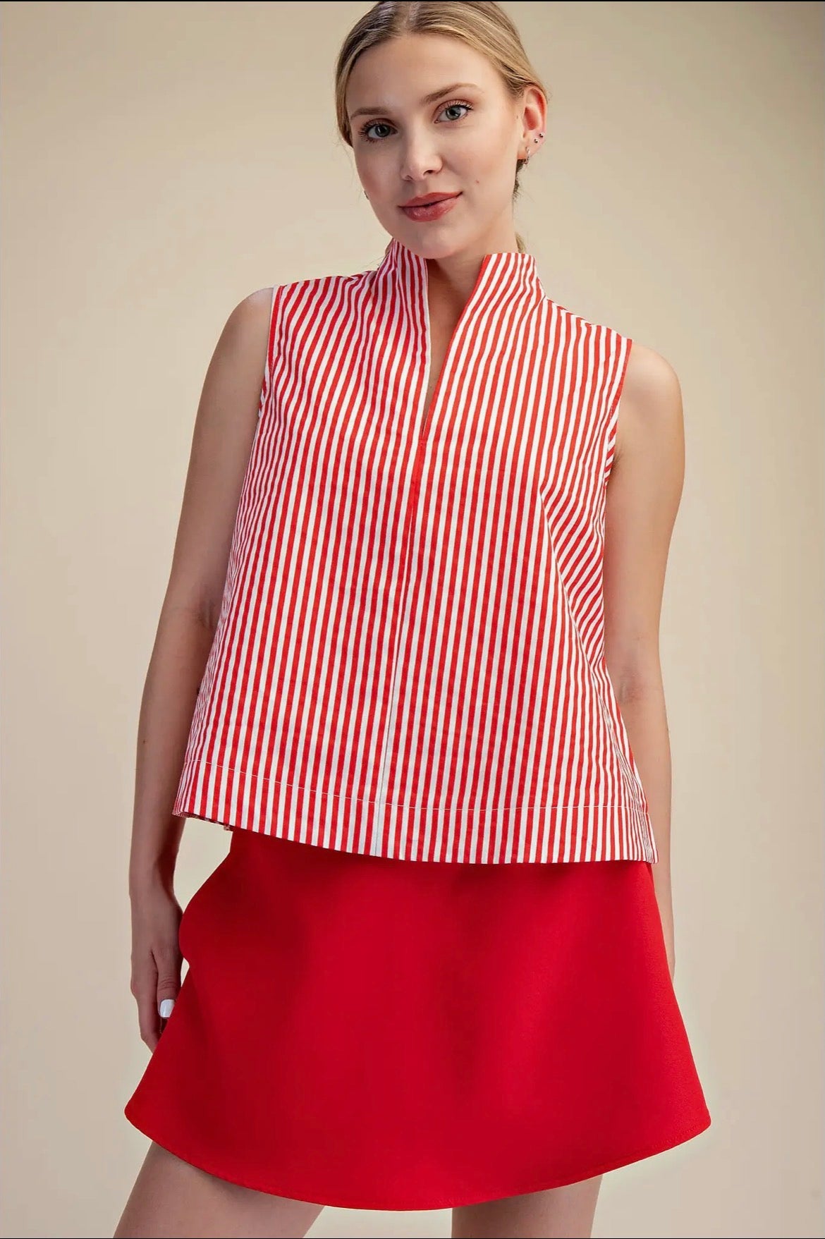 Woman wearing a red and white striped sleeveless top with a red skirt on a beige background