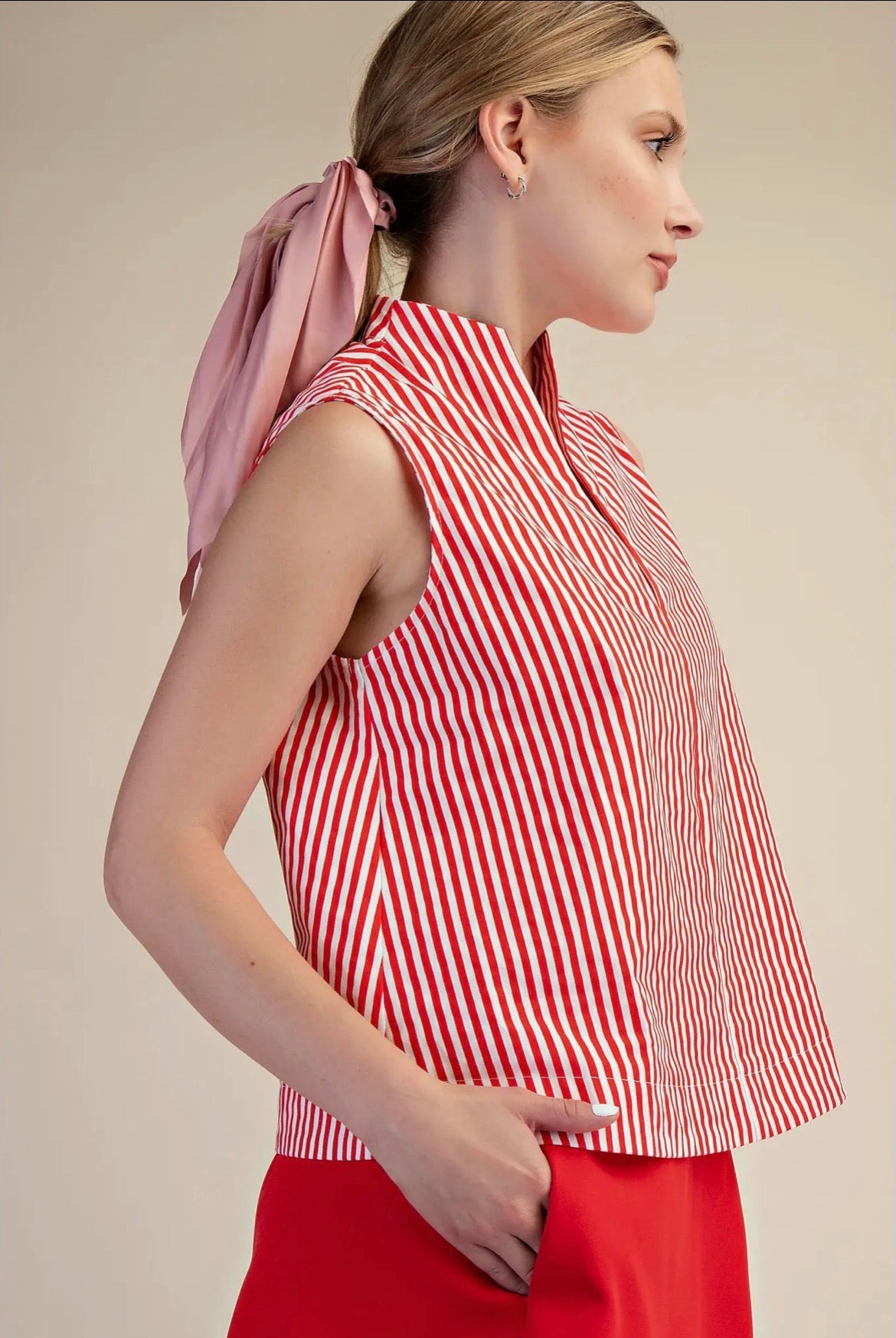 Woman wearing a red and white striped sleeveless top with a pink scarf, on a beige background