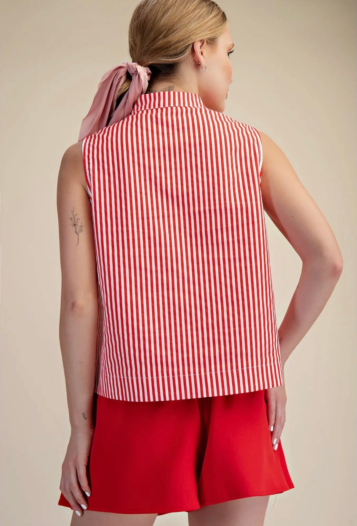 Woman wearing a red and white striped sleeveless top and red shorts on a beige background