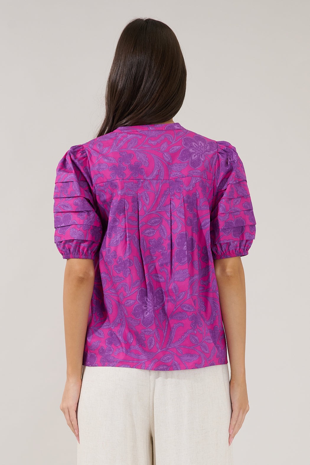 Person wearing a pink and purple patterned blouse against a plain background