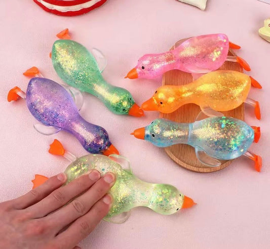 Colorful glittery duck toys on a pink surface with a hand touching one of them.