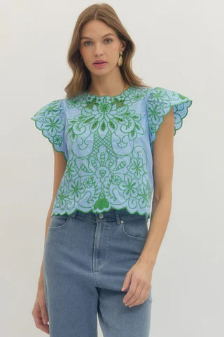 Woman wearing a light blue top with green floral embroidery and high-waisted jeans on a white background