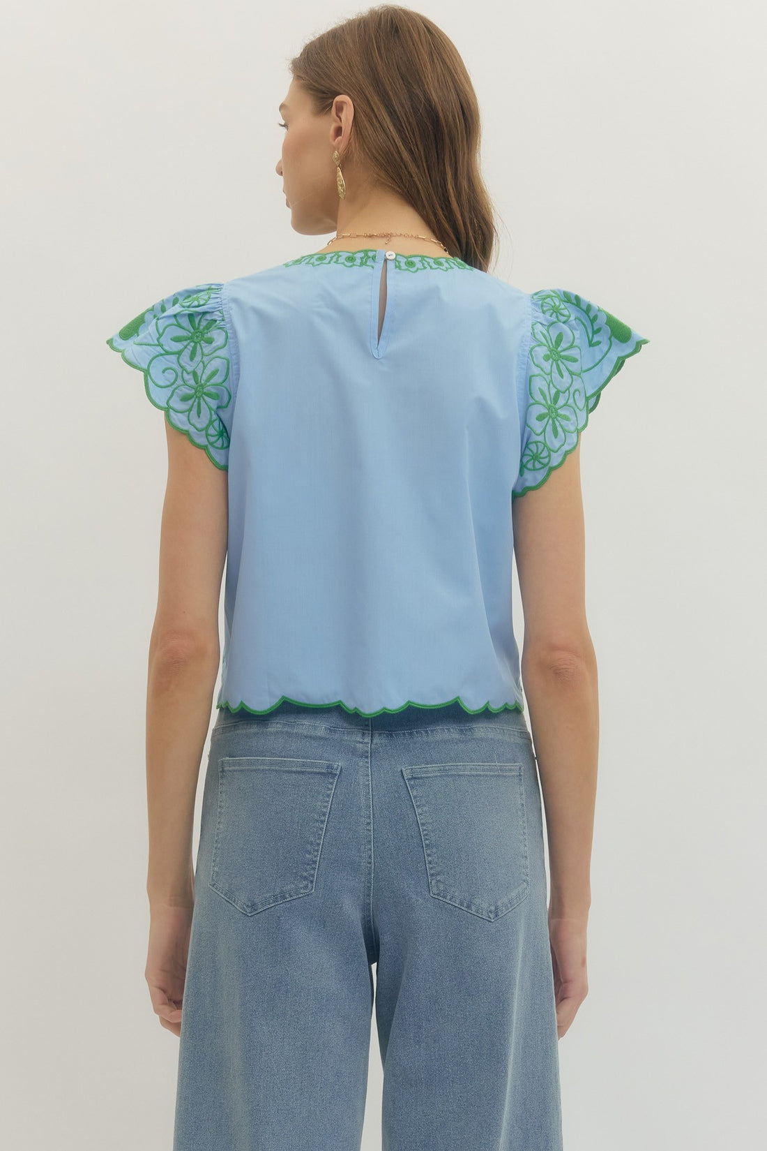 Woman wearing a light blue top with green floral patterns on a plain background