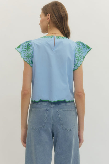 Woman wearing a light blue top with green floral patterns on a plain background