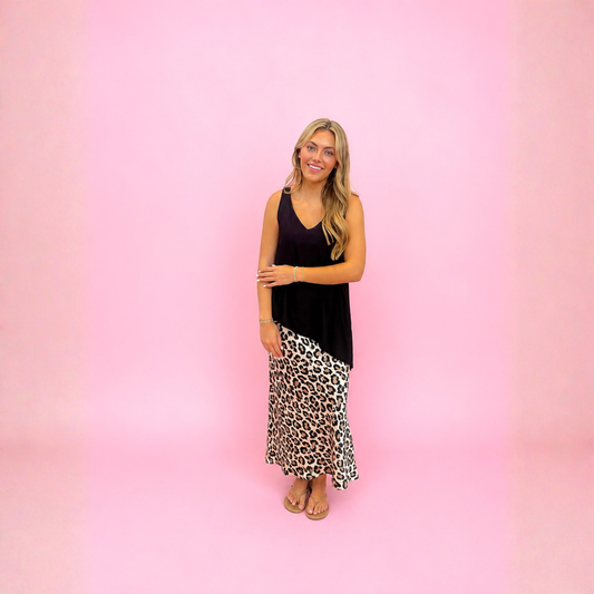 A woman modeling a two-piece outfit consisting of a black sleeveless top and a leopard print maxi skirt, standing against a solid pink background.