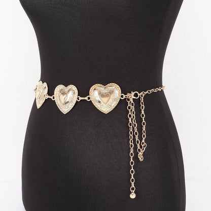 A gold-toned chain belt with three textured heart-shaped links and dangling chain accents, displayed on a black mannequin torso against a white background.