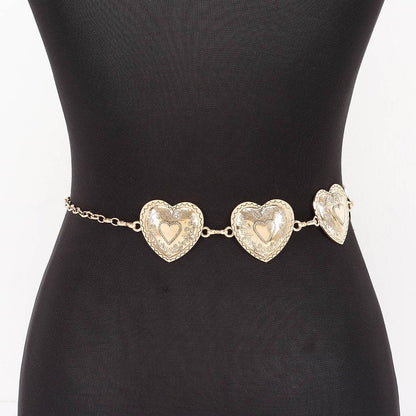 A gold heart chain belt with three textured heart charms displayed on a black mannequin torso.