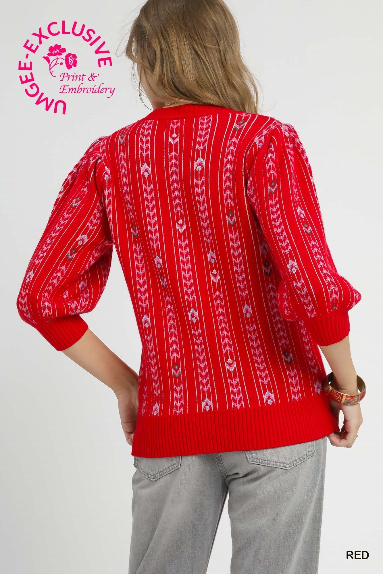 Back view of a red embroidered sweater featuring puff sleeves and ribbed trim, styled with light wash jeans and a gold bangle bracelet.