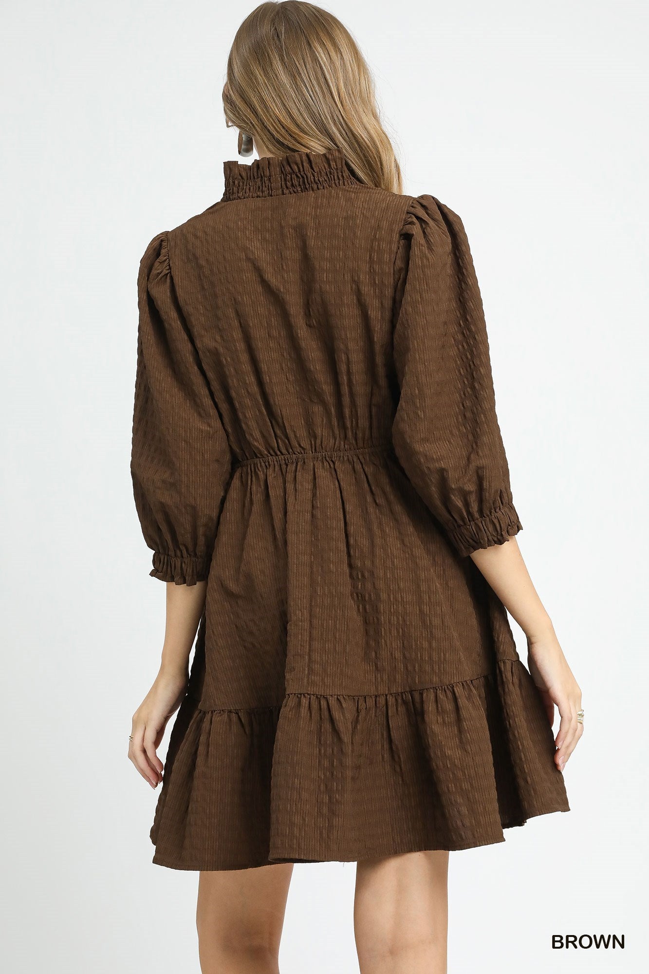 Back view of a brown mini dress featuring a gathered waist, puff sleeves with ruffled cuffs, and a flared tiered hem in a textured fabric