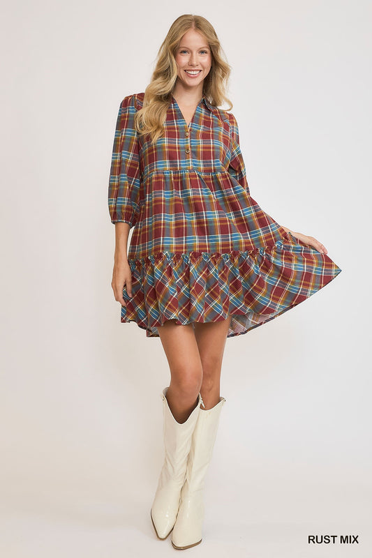 Model wearing a rust mix plaid mini dress with a ruffle hem, button neckline, and puff sleeves, styled with white knee-high boots against a light background.