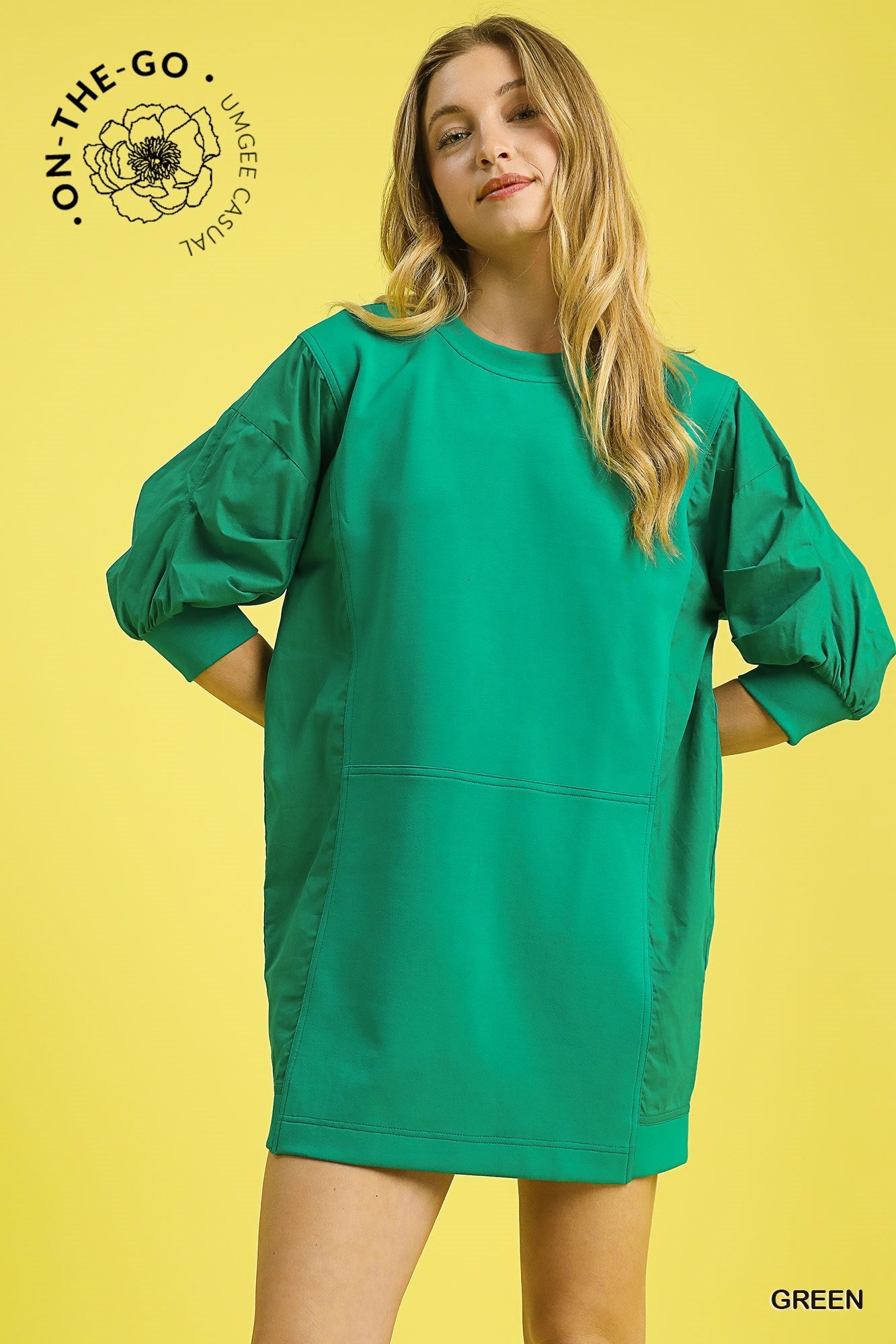 Model wearing a vibrant green pullover sweatshirt dress with puff sleeves, relaxed fit, and sporty seaming detail, styled with a silver cuff bracelet and striped socks for a fun, casual look.