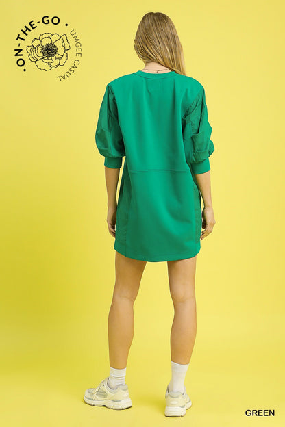 Model wearing a vibrant green pullover sweatshirt dress with puff sleeves, relaxed fit, and sporty seaming detail, styled with a silver cuff bracelet and striped socks for a fun, casual look.