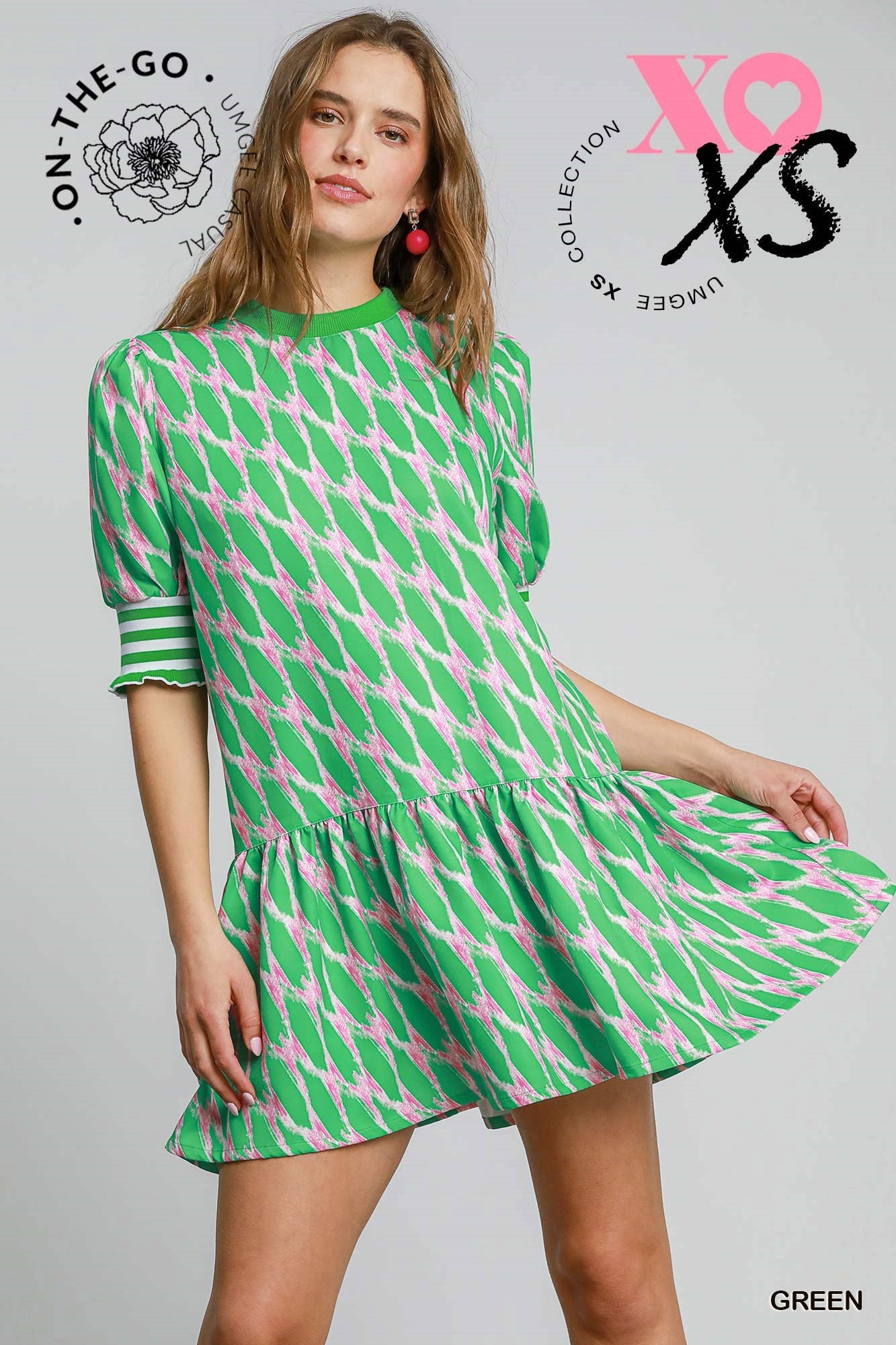 Model wearing a vibrant green and pink printed mini dress with puff sleeves and striped cuffs, featuring a tiered skirt and a playful, preppy silhouette.
