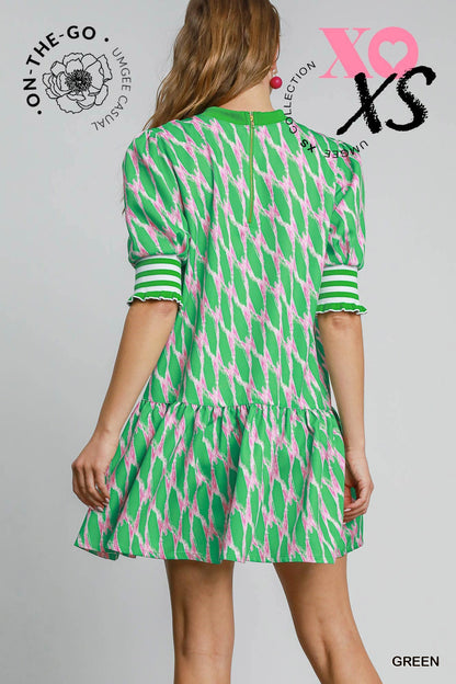 Model wearing a vibrant green and pink printed mini dress with puff sleeves and striped cuffs, featuring a tiered skirt and a playful, preppy silhouette.