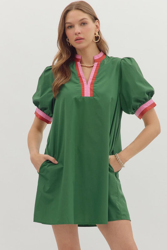 Model wearing a green mini dress with puff sleeves and a deep V colorblock neckline in pink and red; features side pockets and a relaxed fit.