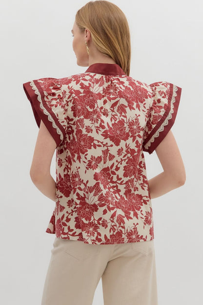Back view of a floral print blouse featuring ruffle-trimmed flutter sleeves and a relaxed fit, styled with neutral pants.