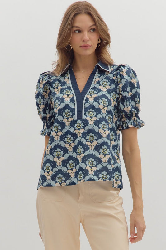 Woman wearing a navy, blush, and sage retro floral puff sleeve blouse with V-notch neckline and smocked cuffs, styled with beige trousers – Milo & Lily Boutique.