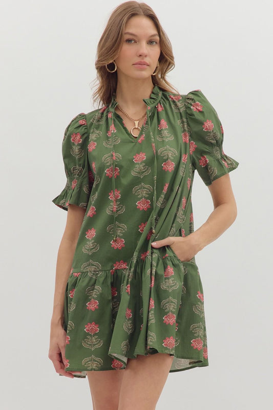 Woman wearing the Olive Blossom Tiered Mini Dress, an olive green puff sleeve dress with pink floral print, ruffled mock neckline with tie detail, tiered hem, and side pockets – Milo & Lily Boutique.