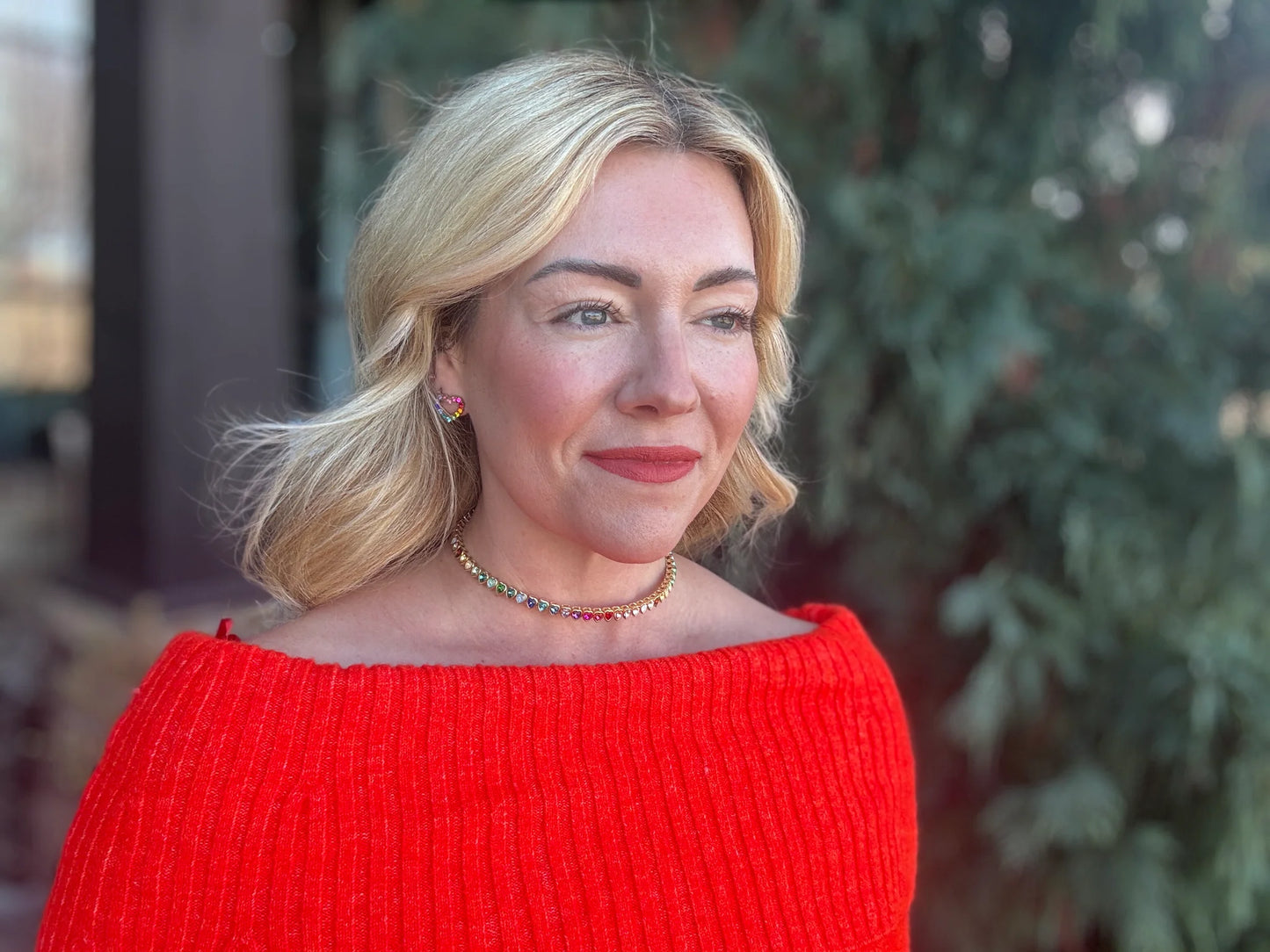 Woman in red off-shoulder sweater with colorful choker necklace and heart earrings outdoors