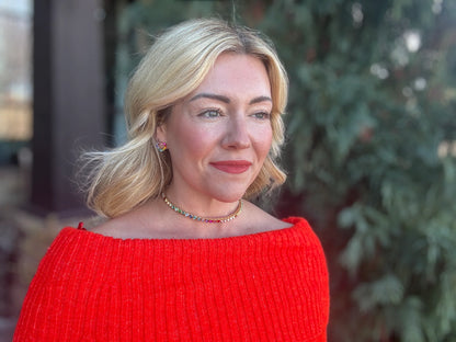 Woman in red off-shoulder sweater with colorful choker necklace and heart earrings outdoors