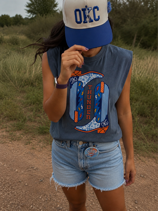 Person wearing a blue sleeveless shirt with a graphic design and denim shorts outdoors.