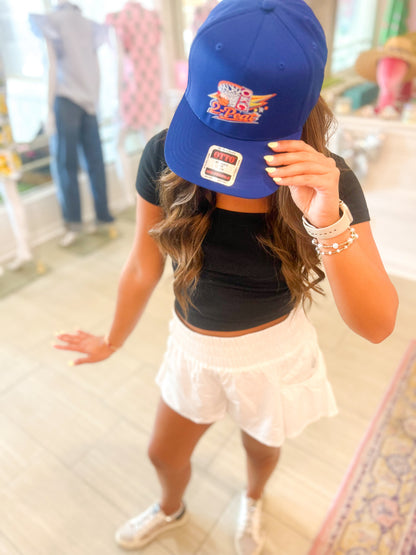 Person wearing a blue cap with a logo, black crop top, and white skirt indoors.