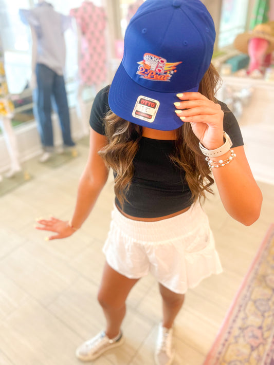 Person wearing a blue cap with a logo, black crop top, and white skirt indoors.