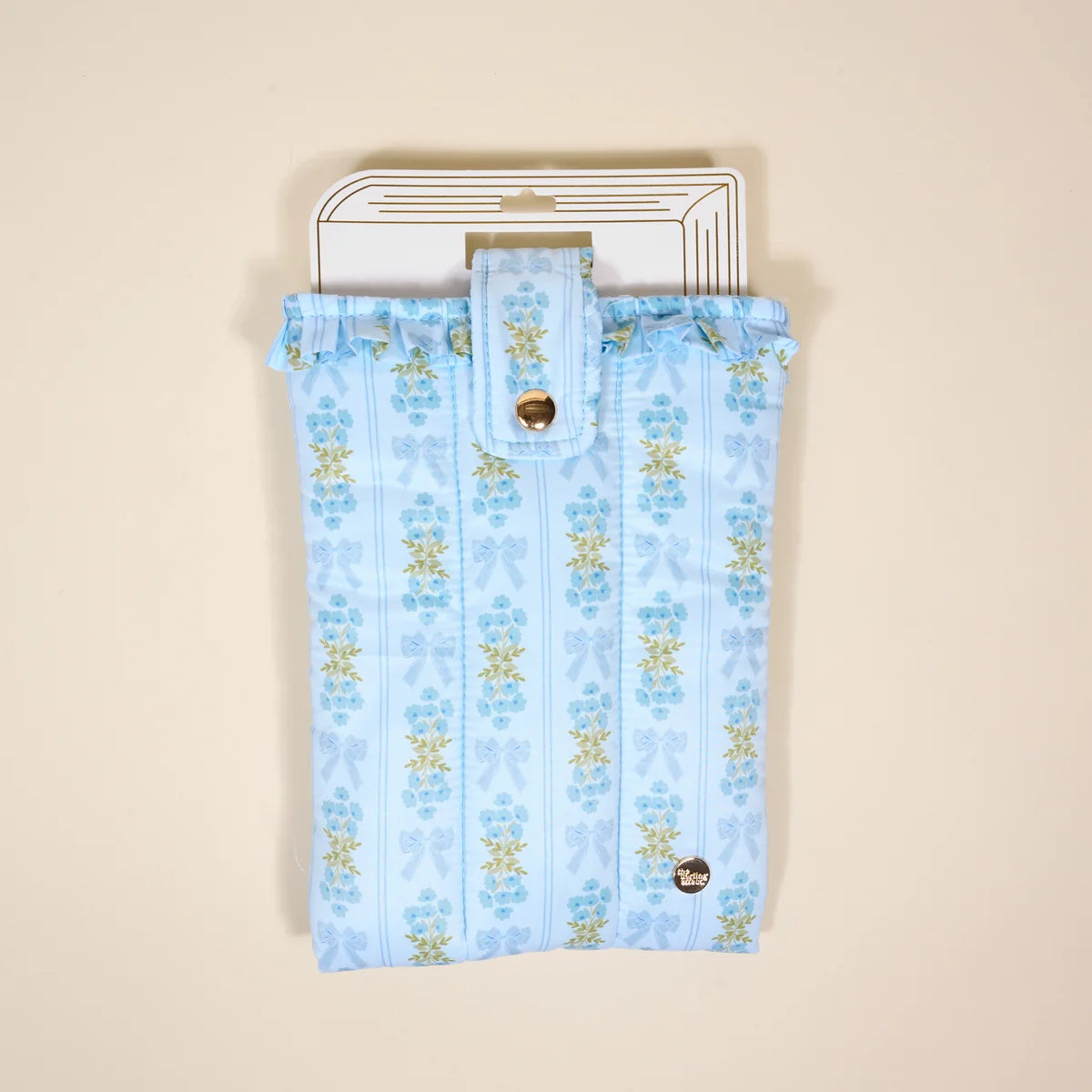 A light blue fabric pouch with a vertical floral pattern in blue and yellow, featuring a ruffled top edge, a snap-button closure flap, and a white cardboard hanger, shown against a solid beige background.