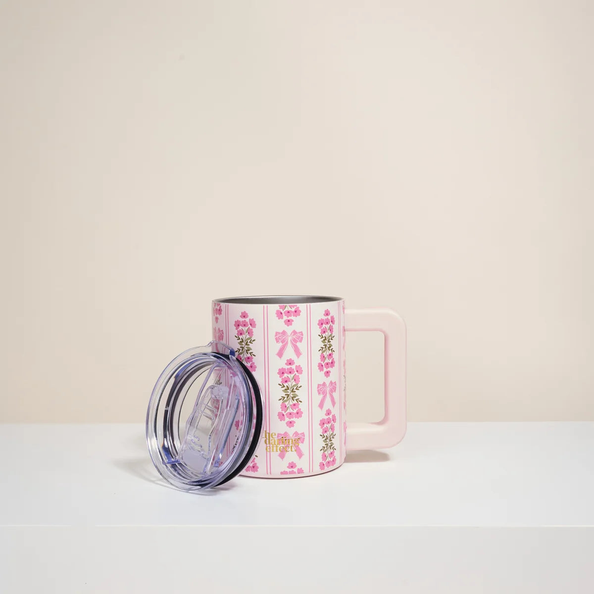 Pink mug with floral design and clear lid on a light beige background