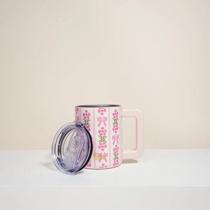 Pink mug with floral design and clear lid on a light beige background