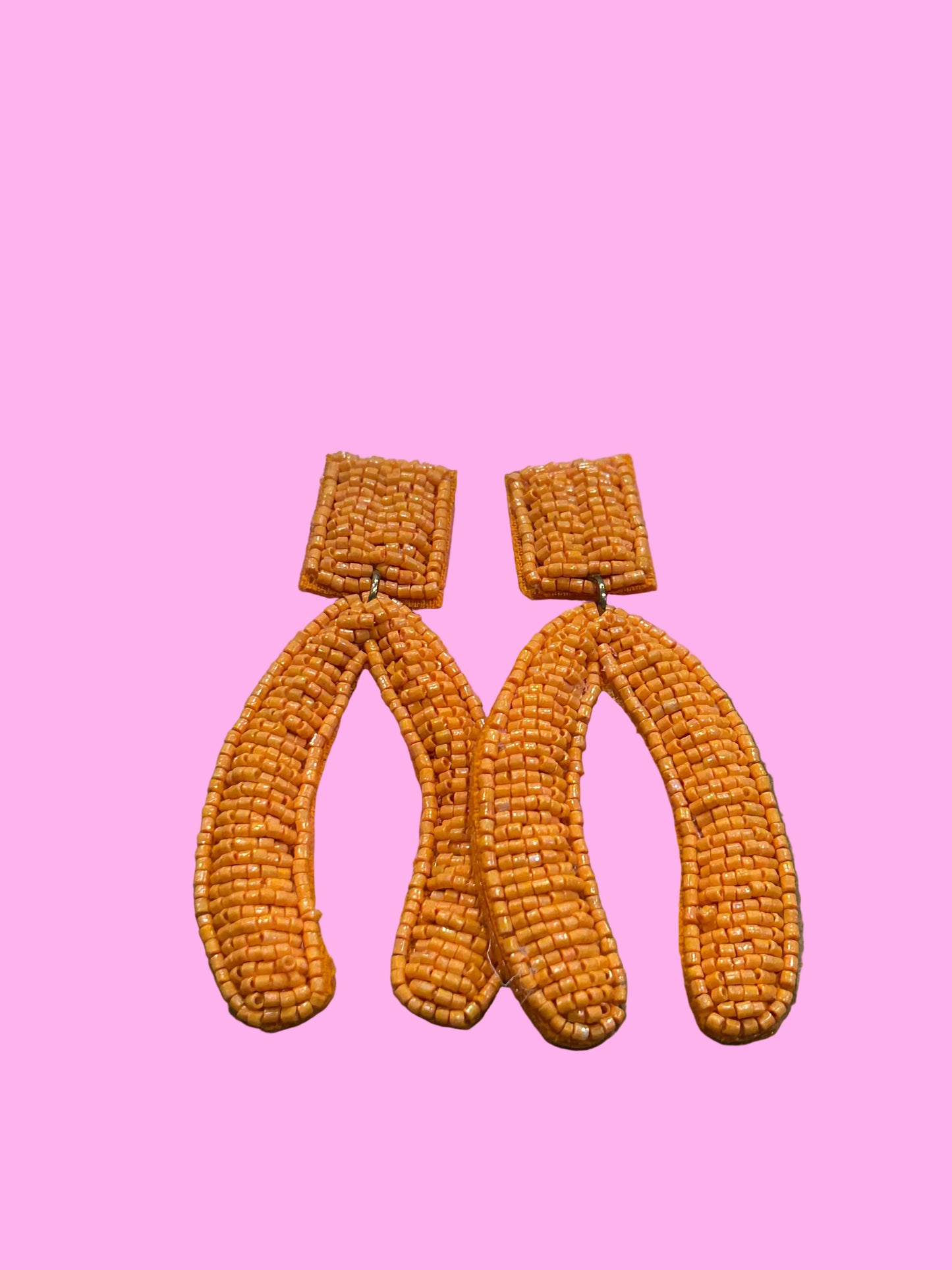 A pair of orange beaded headbands with matching small beaded pouches, displayed on a pink backing card against a textured brown background.