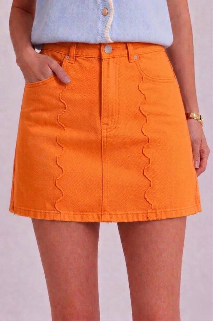 Person wearing an orange denim skirt with a plain background