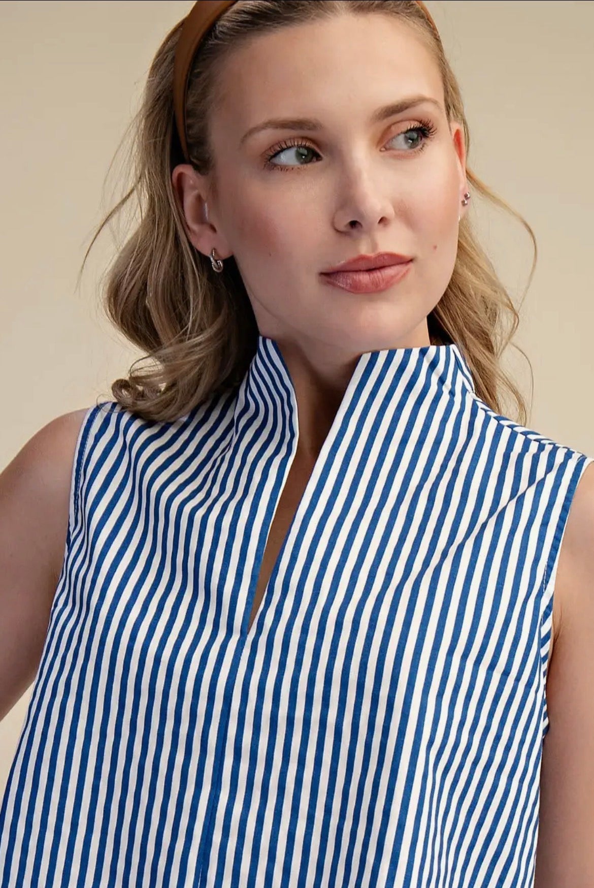 Woman wearing a blue and white striped sleeveless top against a beige background