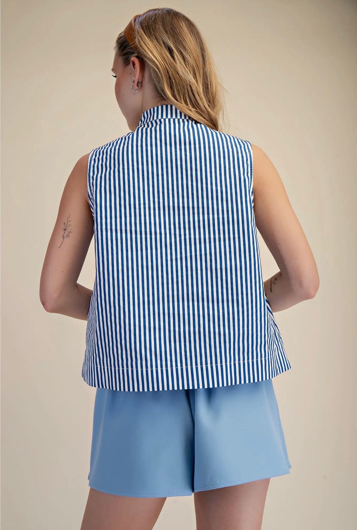 Person wearing a blue and white striped sleeveless top and light blue shorts on a beige background
